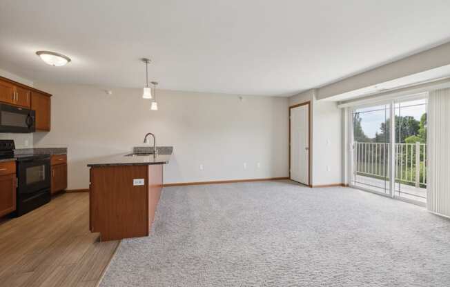 an empty living room with a kitchen and a large window