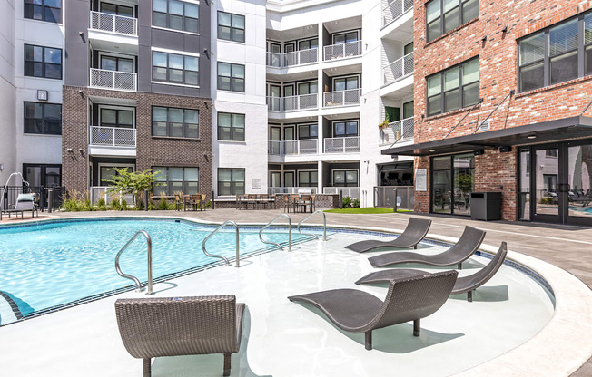 a swimming pool with chairs in front of an apartment building