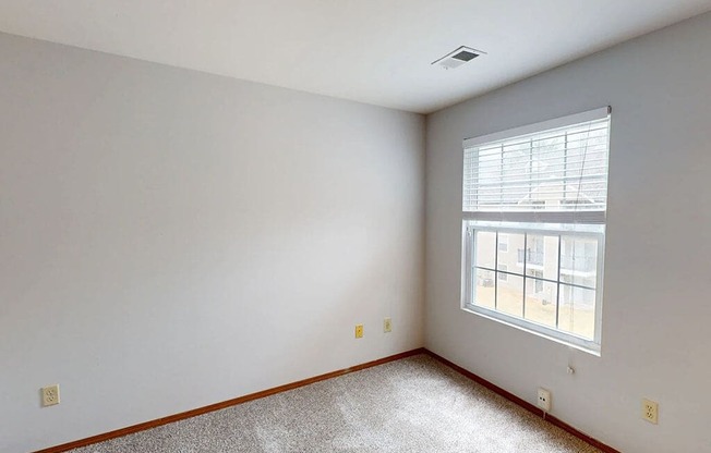 A room with a window and a carpeted floor.