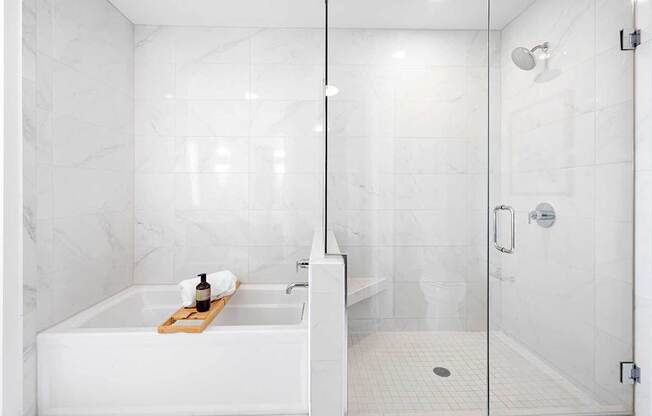 A white bathroom with a marble wall and a glass shower door.