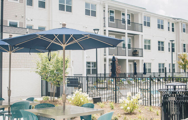 a patio with tables and umbrellas in front of an apartment building