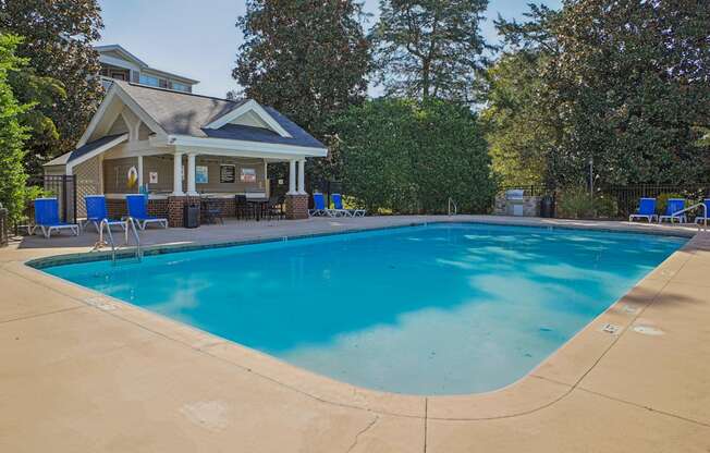 A large swimming pool in front of a house with a covered patio.