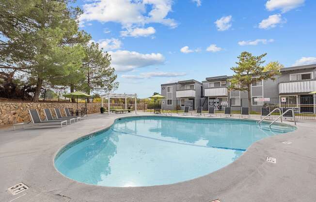A large outdoor swimming pool surrounded by trees and a building in the background.