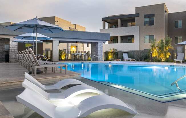 a swimming pool with lounge chairs and umbrellas in front of a building