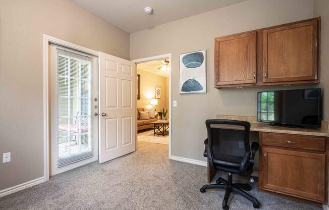a room with a desk and a chair and a door leading to a living room