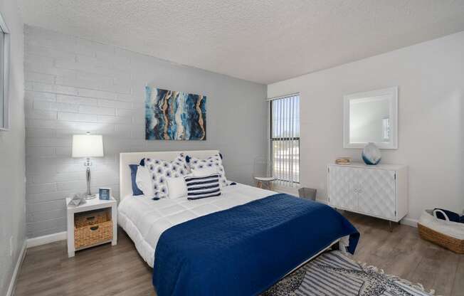 Luxury Studio Apartments In Phoenix, AZ - Crosstown Phoenix - Spacious Bedroom With Wood-Inspired Flooring, White Brick Walls, And Floor-To-Ceiling Window.