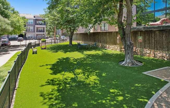 A green lawn with a tree in the middle and a fence around it.