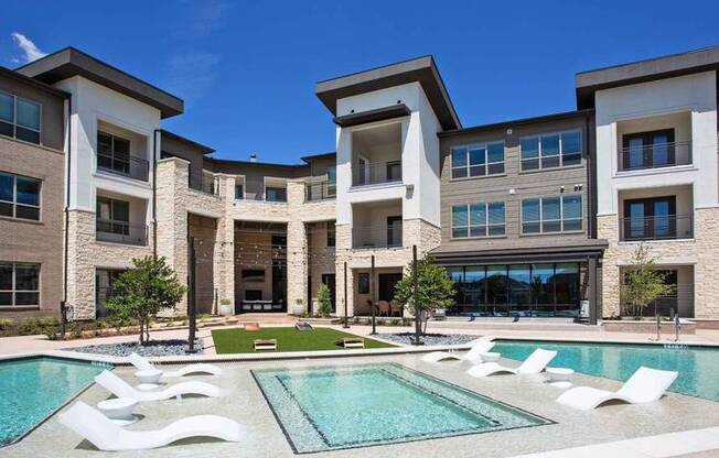 a pool with white chairs in front of an apartment building at Hunters Creek Apartments, Denton Texas