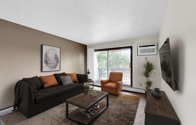A living room with a black couch, orange pillows, a coffee table, and a flat screen TV mounted on the wall.