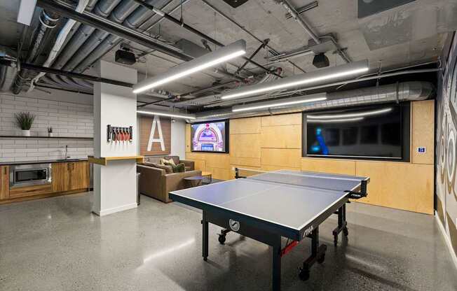 A ping pong table is in the middle of a room with a TV and a bar.