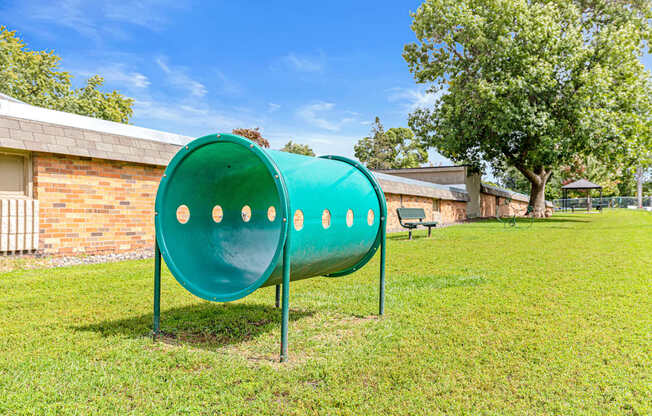 A green tube slide in a grassy area with a building in the background.