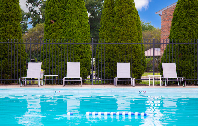 A pool with four chairs and a fence in the background.