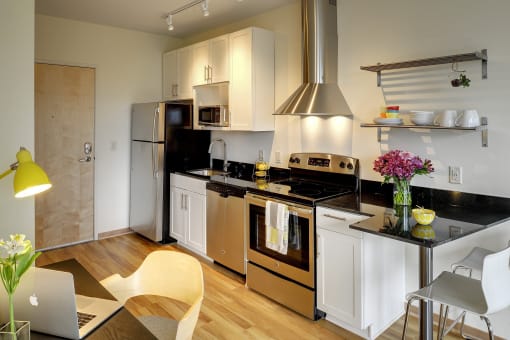 Angled view of kitchen with lights on, stainless steel appliances, white cabinets, black granite counter with breakfast bar