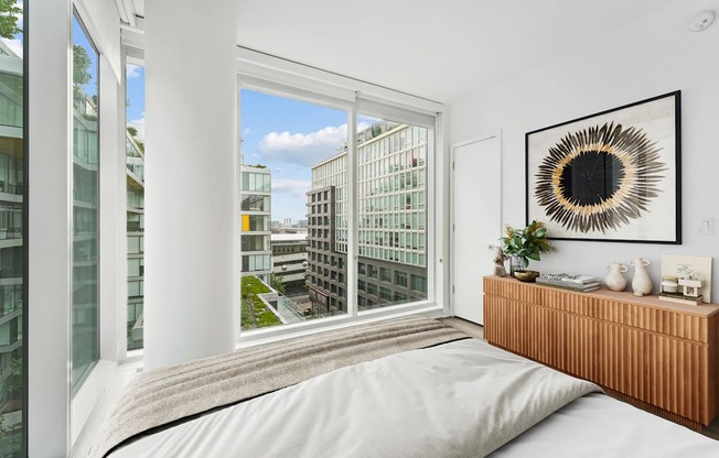 A bedroom with a large window overlooking a cityscape.
