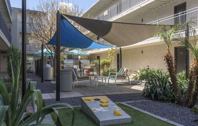 A patio with a blue shade sail and a concrete table with yellow bowls on it.
