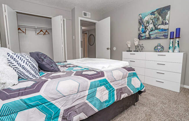 Model bedroom with a bed, dresser, and closet at Maplewood apartments in Shreveport, LA.