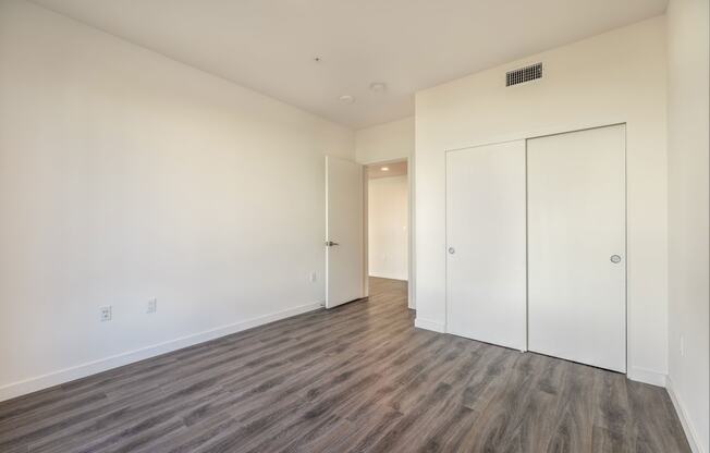 a bedroom with white walls and wood flooring and a closet