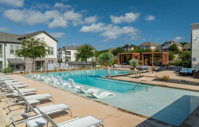 A pool with sun loungers and a building in the background.