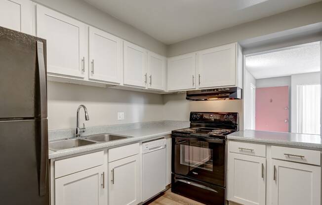A kitchen with white cabinets and a black refrigerator.