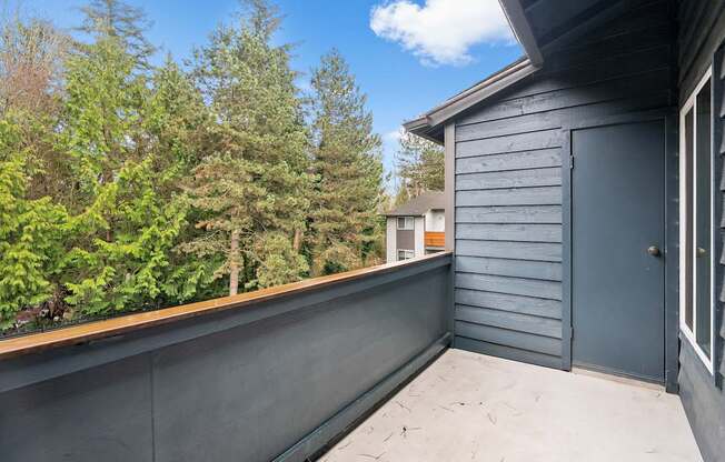 A grey deck with a door and a window overlooking a forest.