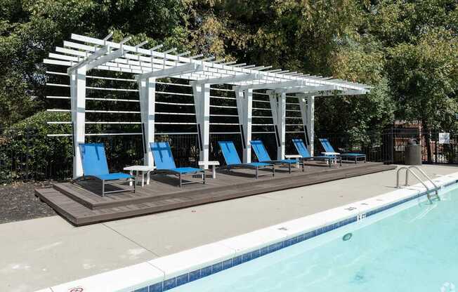 A pool with a white pergola and blue lounge chairs.
