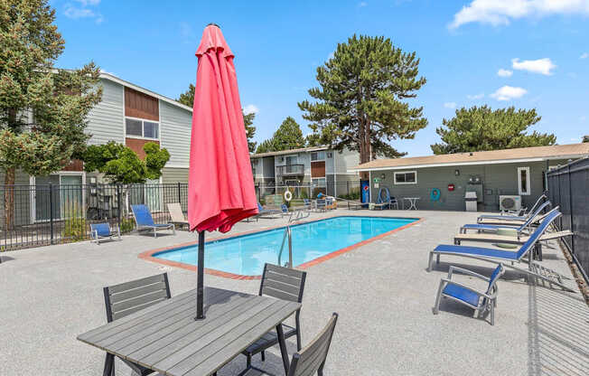 A red umbrella is on a table next to a large blue swimming pool at Wildflower in Kennewick, WA.