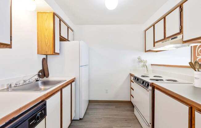 A double galley kitchen with white appliances and wooden cabinets at Shiloh Glen Apartments in Bilings.