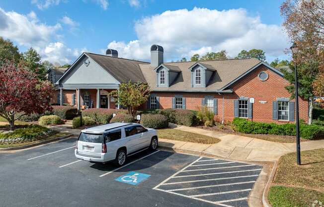 A silver minivan is parked in a handicapped spot in front of a brick building.