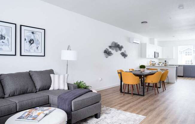 a living room with a couch a table and chairs and a kitchen in the background