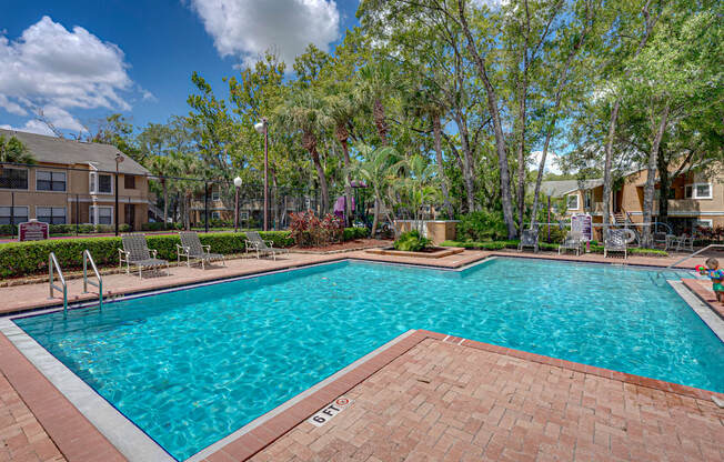 A large swimming pool surrounded by trees and a brick patio.