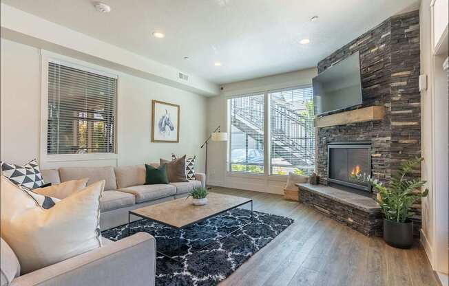 A modern living room with a grey couch, a fireplace, and a TV mounted on a stone wall at Forestplace Apartment Homes, Forest Grove