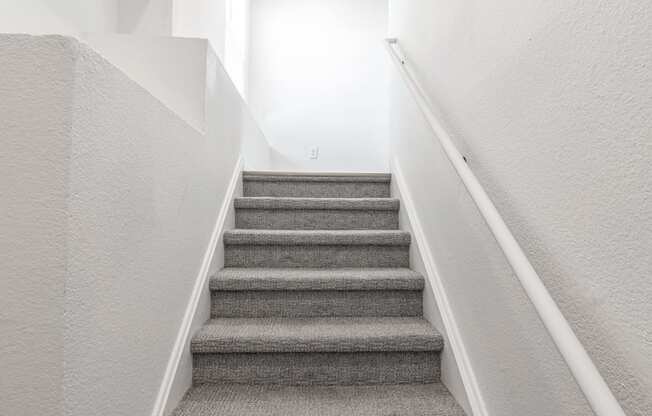 a staircase with grey carpeting and white walls and a white railing with a white