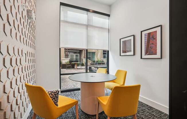 A white table with two yellow chairs in front of a white wall with a patterned wallpaper.