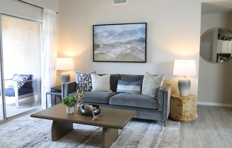 A living room with a grey couch, a coffee table, and a painting on the wall.