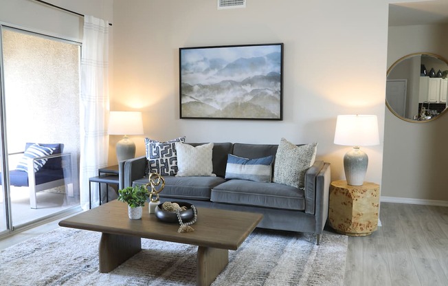 A living room with a grey couch, a coffee table, and a painting on the wall.