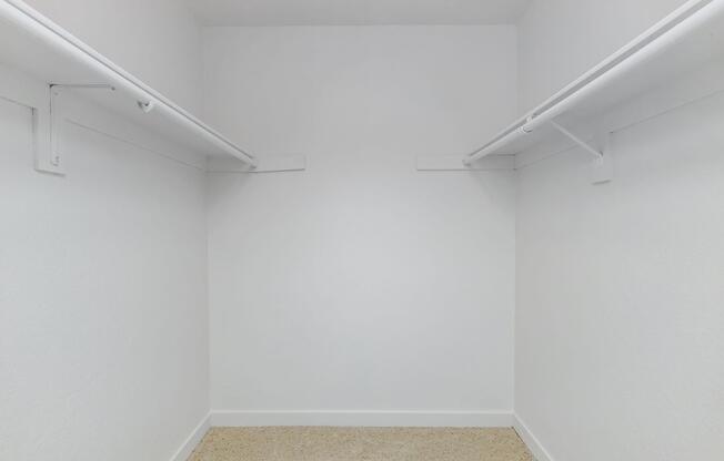 A spacious, empty closet with white walls and two hanging rods. The floor is carpeted, and there are no items or furnishings present, creating a minimalist and clean appearance.