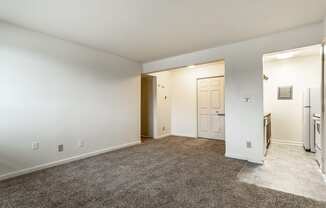 an empty living room with white walls and carpet and a door to a kitchen at Pheasant Run in Lafayette, IN 47909