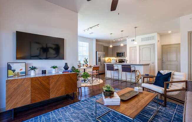 A modern living room with a wooden cabinet, a blue rug, and a ceiling fan.