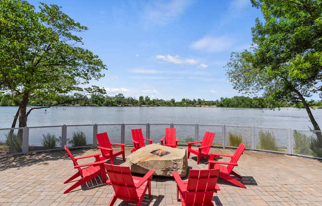 A table surrounded by red chairs is on a patio overlooking a body of water.