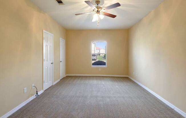 A room with a ceiling fan and a window showing a house.