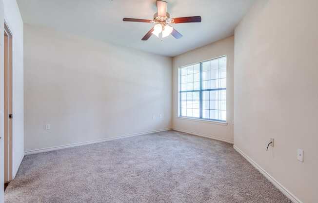 an empty living room with a ceiling fan and a window