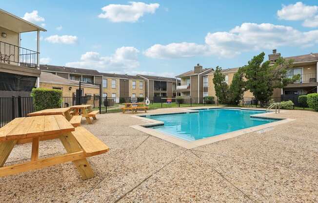 A pool surrounded by picnic tables and apartment buildings.