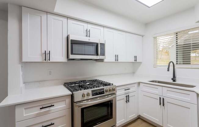 A modern kitchen with white cabinets and a stainless steel stove top.