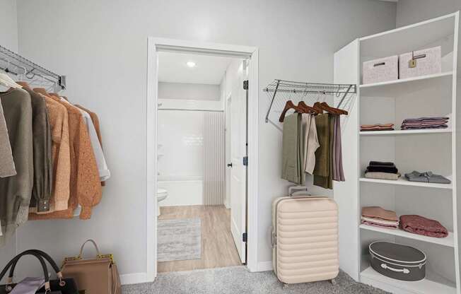 A white closet with clothes and a suitcase.