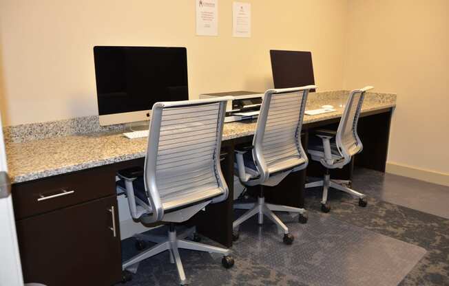a large desk with four chairs and two computer monitors