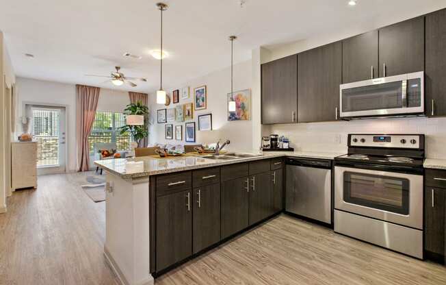San Marcos Apartments-Sadler House-Kitchen-Stainless Steel Appliances, Dark Wood Cabinets, Grey Floors, and Hanging Light Fixtures.
