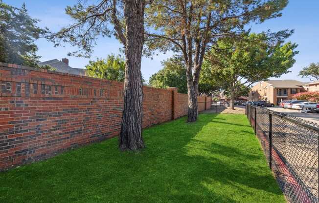 a brick retaining wall with trees and a chain link fence
