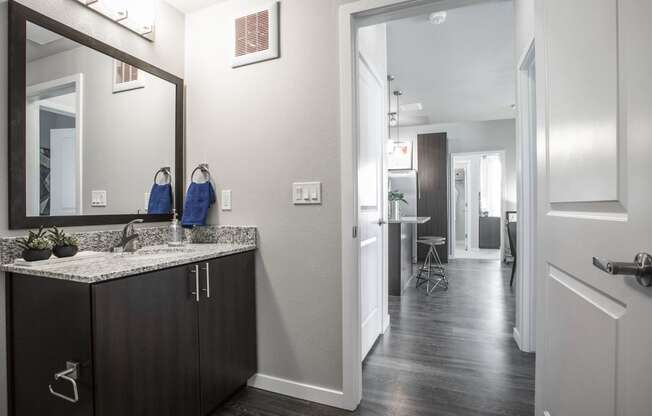 Bathroom with large mirror and dark cabinets, granite countertop, door open to apartment hallway