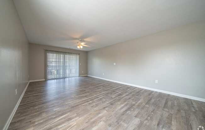 the spacious living room with wood flooring and a ceiling fan