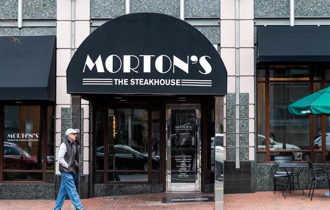 a man walking in front of a mottos the steakhouse restaurant